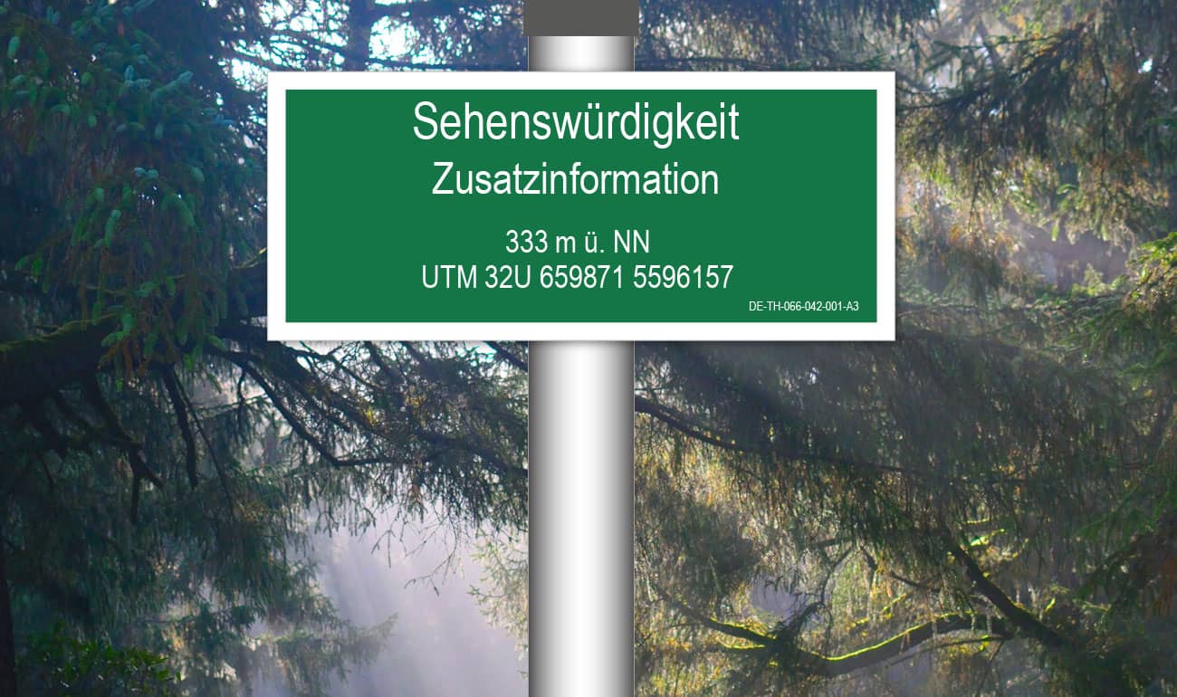 grünes, rechteckiges Schild mit weißer Schrift im Hintergrund Wald